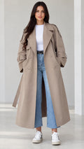 Front view of model wearing beige longline belted trench coat with jeans and white sneakers